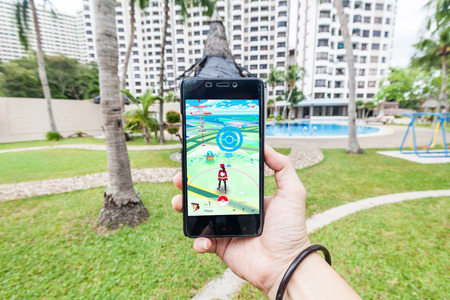 California, United States, 16 July 2016 : Hand holding a cellphone to play Pokemon Go with blur garden backgroundのeditorial素材