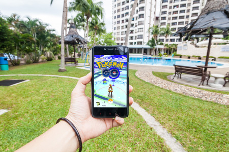 California, United States, 16 July 2016 : Hand holding a cellphone to play Pokemon Go with blur garden backgroundのeditorial素材