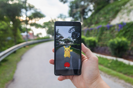 California, United States - July 23, 2016: Close up of a man holding a smartphone while playing Pokemon Go game and try to catch a Pokemonのeditorial素材