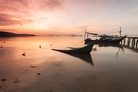 Sunrise by the shore with silhouette of broken boatの写真素材
