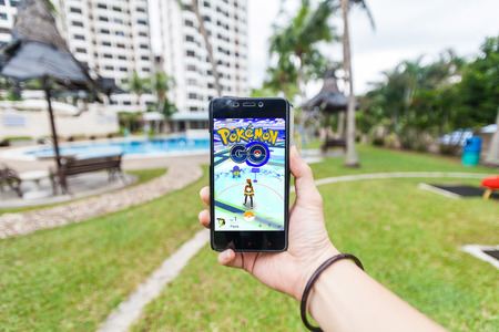 California, United States - July 16, 2016: Hand holding a cellphone to play Pokemon Go with blur garden backgroundのeditorial素材