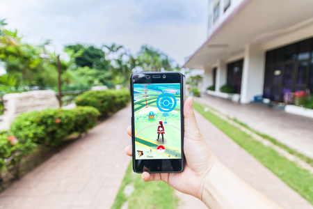 California, United States - July 16, 2016: Hand holding a cellphone to play Pokemon Go with blur garden backgroundのeditorial素材
