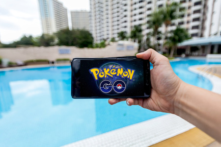 California, United States - July 16, 2016: Hand holding a cellphone to play Pokemon Go with blur garden backgroundのeditorial素材