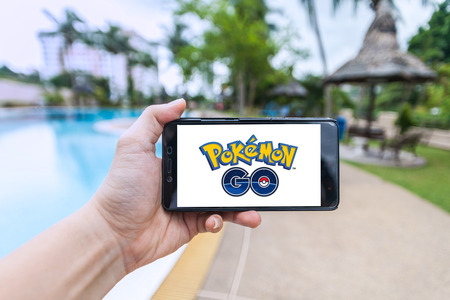 California, United States - July 16, 2016: Hand holding a cellphone to play Pokemon Go with blur garden backgroundのeditorial素材