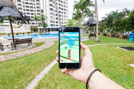 California, United States - July 16, 2016: Hand holding a cellphone to play Pokemon Go with blur garden backgroundのeditorial素材