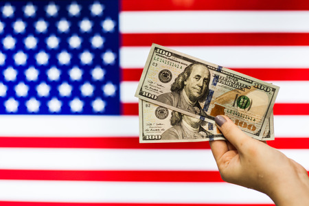 Man holding US Dollar bank note indicating market crash due to new US president with flag backgroundの写真素材