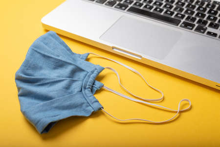 Blue facemask and laptop over mustard yellow table