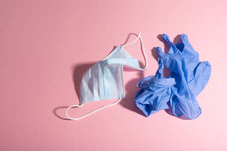 Used blue nitrile gloves and disposable facemask over pink background