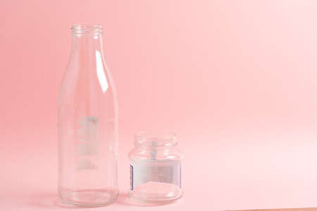 A bottle and a jar made of glass reused with blank space on the top right over pink background deskの写真素材