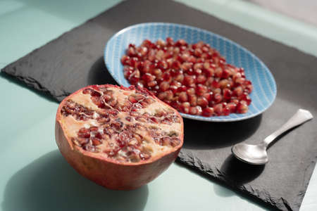 Half pomegranate and seeds on dish still on aqua menthe desk on sun light