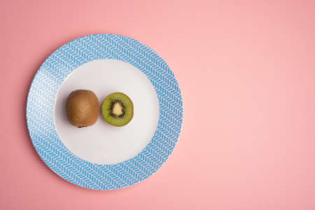 Kiwi and a half on blue and white dish over pink table flat layの写真素材