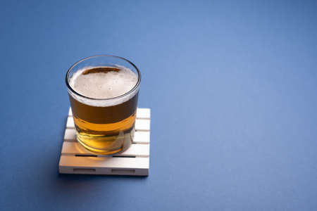 Glass of blonde beer on small white pallet over marine blue desk. Drinking, watching TV snackの写真素材