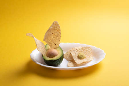 Mexican snack concept by raw ingredients guacamole over a mustard yellow desk