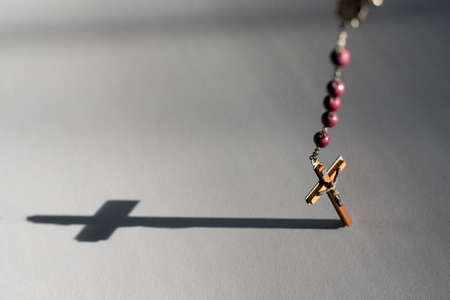 Rosary hanging over white surface projecting cross shadow and gray shade copy space. Background ready for mass schedule posterの写真素材