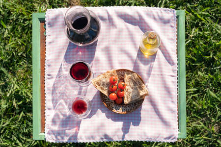 Mediterranean food picnic flat lay in garden at sunset. Red wine, olive oil, tomatoes and bread over...
