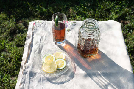 Refreshing ice tea in the garden at sunset. Linen tablecloth with glass, bottle and dish with lime unripe orange and lemon slices. Citric vibes and copy space availableの写真素材