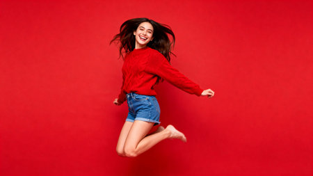 Woman jumping in red sweater against red backgroundの素材