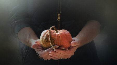 Halloween pumpkin in the hands of a man in a black dress