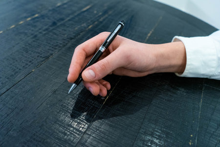 Close-up of a woman's hand writing on a black wooden tableの写真素材