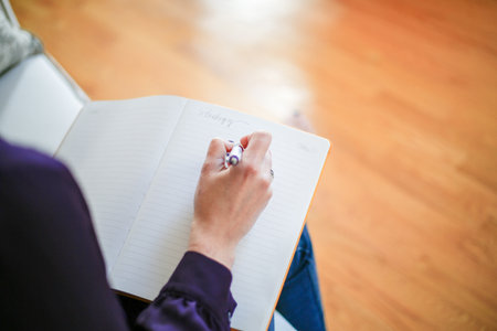 Close up of female hands writing in notebook while sitting on floor at homeの写真素材
