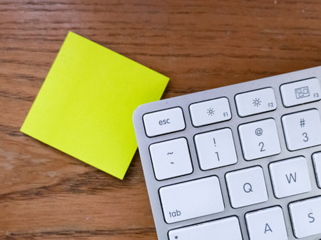 Keyboard and yellow sticky note on wood background with copy space.