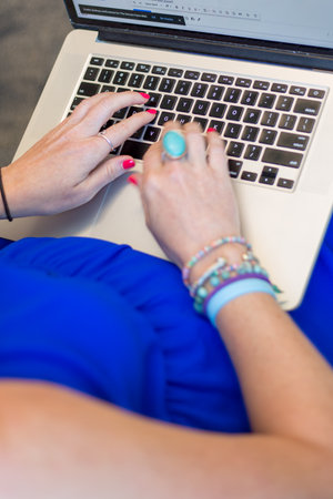 Close up of female hands typing on laptop keyboard. Woman in blue dress working on computer.の写真素材