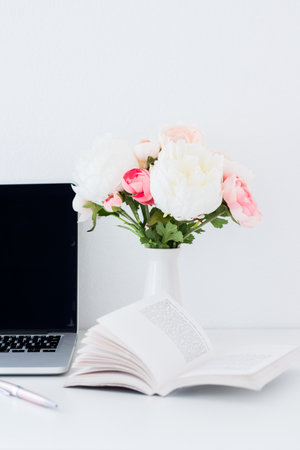 Flowers in vase with notebook and laptop on white wall backgroundの写真素材
