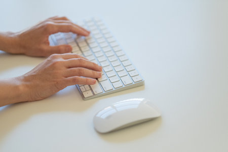 Close up of male hands typing on computer keyboard on white desk.の写真素材