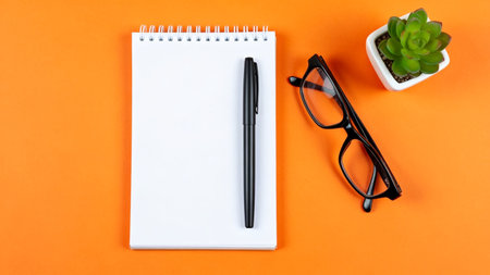 Office desk table with notepad, pen, glasses and plant. Top view with copy spaceの素材