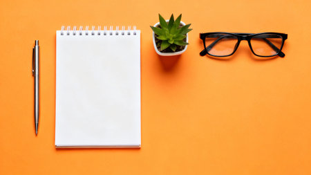 Top view of office desk with notebook, pen and glasses on orange backgroundの素材