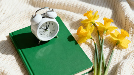 Alarm clock, book and daffodils on knitted backgroundの素材