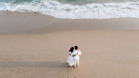 Aerial view of bride and groom holding hands while walking on the beachの素材