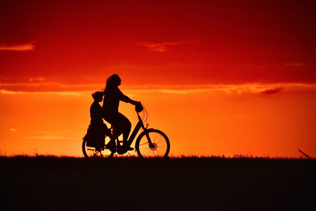 Silhouette of mother and daughter riding bikes at sunset. Concept of healthy lifestyle.の写真素材
