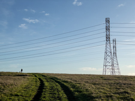 Electricity pylons in the countryside with a person walking on the grassの写真素材