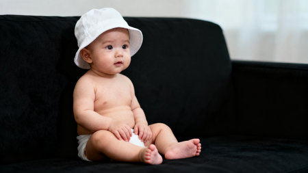Baby wearing white hat on black couchの素材