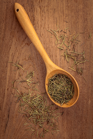 Dried rosemary leaves in wooden spoon on teak wood  background .の写真素材