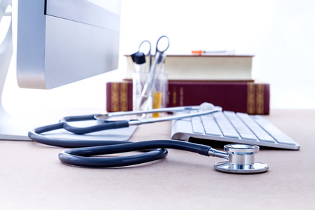 Doctor's desk with computer and medical textbook with shallow depth of field focus on stethoscope .の写真素材