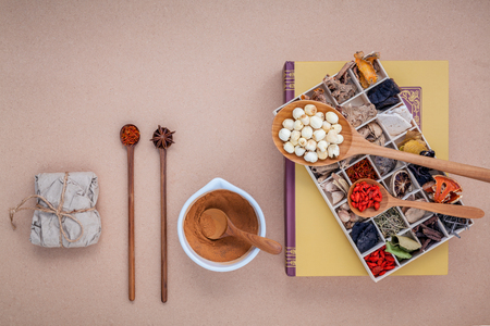 Alternative health care dried various Chinese herbs in wooden box lotus seed and saffron in wooden spoon  on medical textbook with mortar on brown background.の写真素材