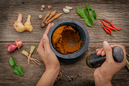 The Women hold pestle with mortar and spice red curry paste ingredient of thai popular food on rustic wooden background.の写真素材