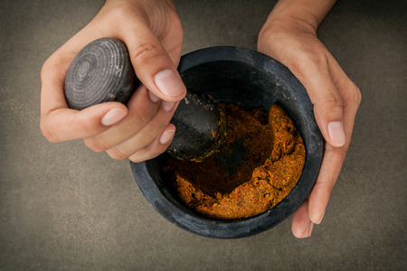 The Women hold pestle with mortar and and spice red curry paste ingredient of thai popular food on dark concrete background.の写真素材