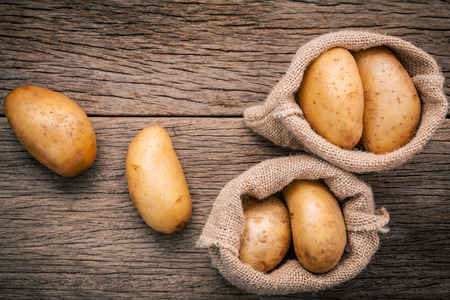 Fresh organic potatoes in hemp sake bag on rustic wooden background.の写真素材