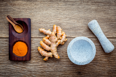 Homemade scrub curcumin powder and curcumin roots with white mortar set up on old wooden background.の写真素材
