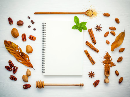 Various nuts pecan, almonds,coffee  beans ,cocoa beans ,cocoa powder ,hazelnuts ,star anise and cinnamon sticks setup with white notebook on white table.の写真素材