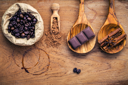 Ingredients for latte coffee . Roasted coffee beans in paper bag  ,chocolate bar ,chocolate powder ,star anise and cinnamon sticks  setup on shabby teak wood background.の写真素材