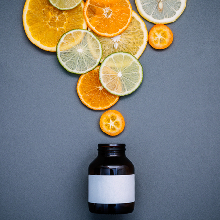 Healthy foods and medicine concept. Bottle of vitamin C and various citrus fruits. Mixed citrus fruits sliced lime,orange and lemon on gray background flat lay.の写真素材