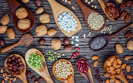 Various legumes and different kinds of nutshells in spoons. Walnuts kernels ,hazelnuts, almond ,brown pinto ,soy beans ,flax seeds ,chia ,chickpea ,red kidney beans and pecan on shabby wooden table.の写真素材