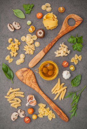 Italian foods concept and menu design.Various kind of pasta with ingredients sweet basil ,tomato ,garlic ,parsley ,champignon and extra virgin olive oil on dark stone background flat lay.の写真素材