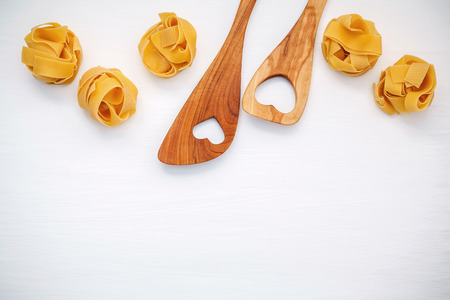 Italian foods concept and menu design. Dried homemade Fettuccine with heart shaped wooden spatula set up on white wooden background with flat lay and copy space.の写真素材