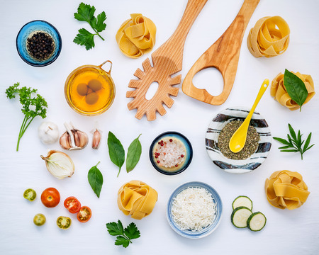 Italian foods concept and menu design. Dried homemade Fettuccine with wooden spatula and  ingredients sweet basil ,tomato ,garlic ,parsley ,bay leaves ,pepper ,zucchini and parmesan cheese flat lay.の写真素材