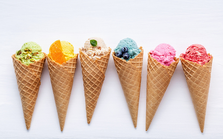 Various of ice cream flavor in cones blueberry ,strawberry ,pistachio ,almond ,orange and cherry setup on white wooden background . Summer and Sweet menu concept.の写真素材